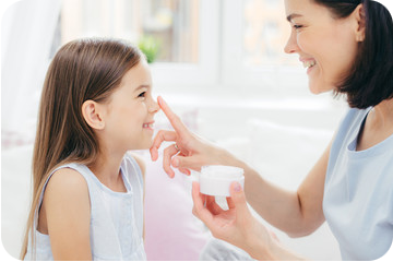Une mère et sa fille se regardent, la mère applique sur le bout du nez de sa fille une crème de sa fabrication maison DIY