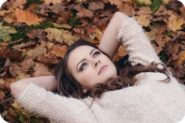 Jeune femme couchée par terre avec les mains derrière la tête sur des feuilles mortes, elle regarde le ciel et réfléchit