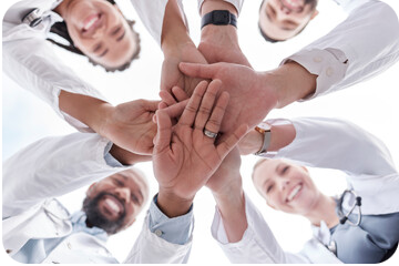 groupe de personnes en cercle vus de dessous, plaçant tous une main au centre en signe de cohésion d'équipe